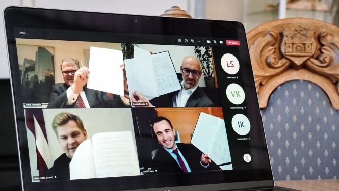 Datora ekrānā cilvēki ar parakstītiem memorandiem rokās