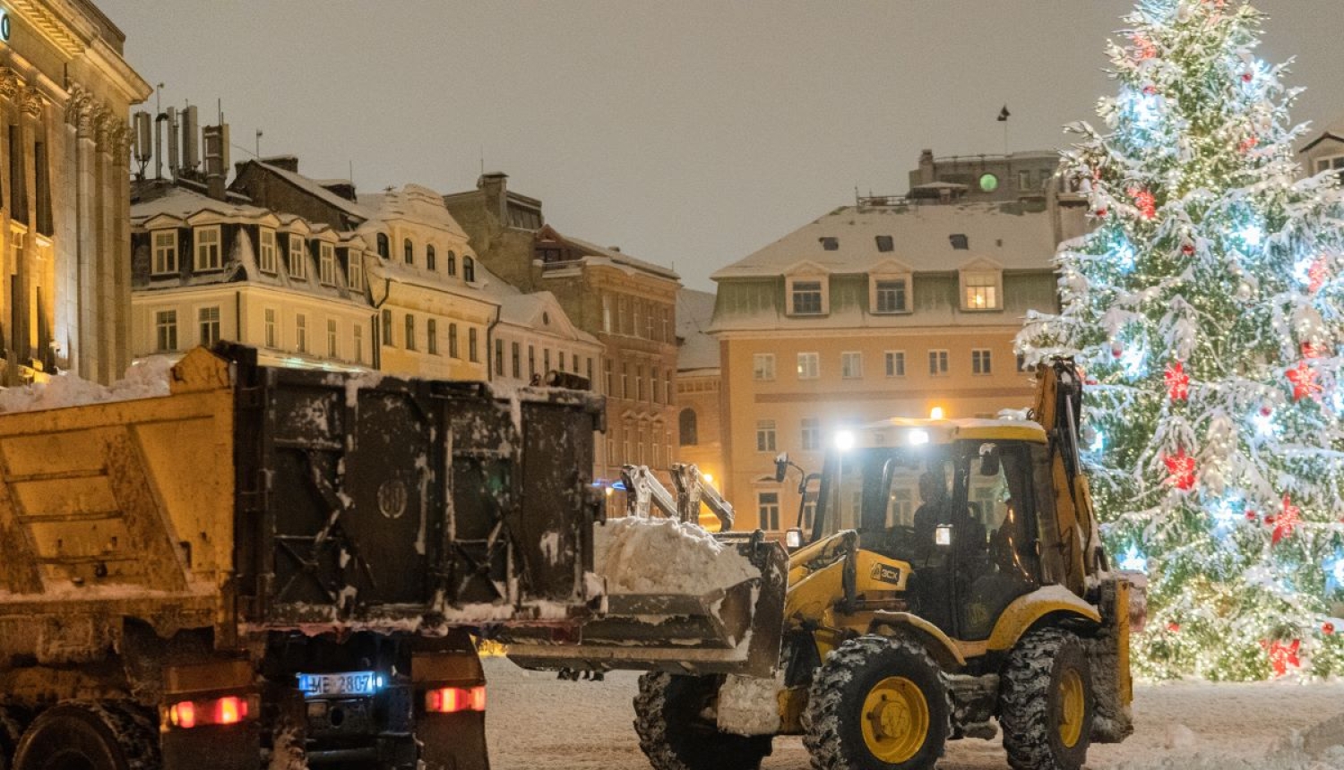Traktors kravas mašīnā krauj sniegu
