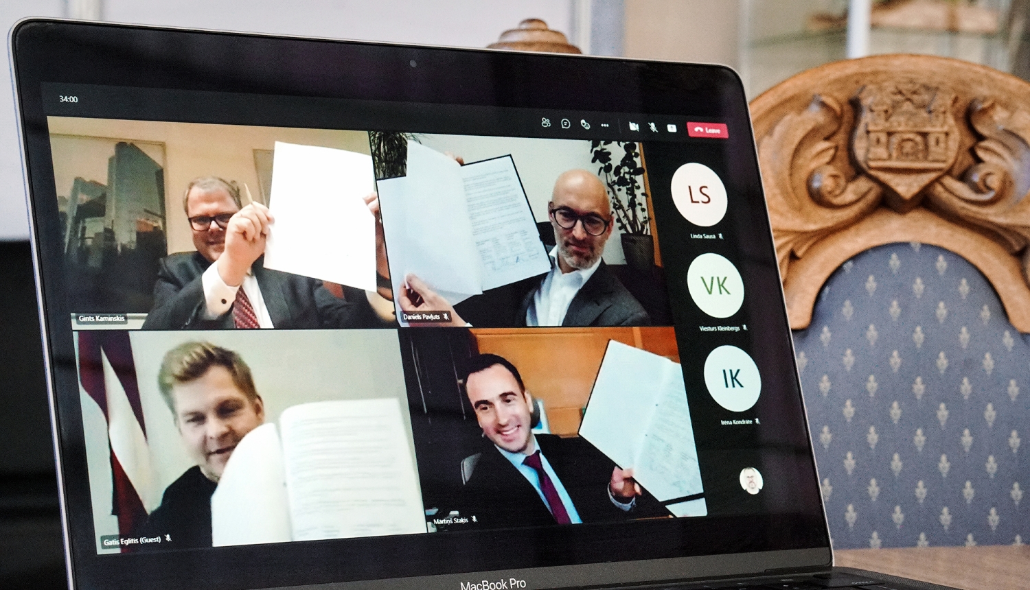 Datora ekrānā cilvēki ar parakstītiem memorandiem rokās